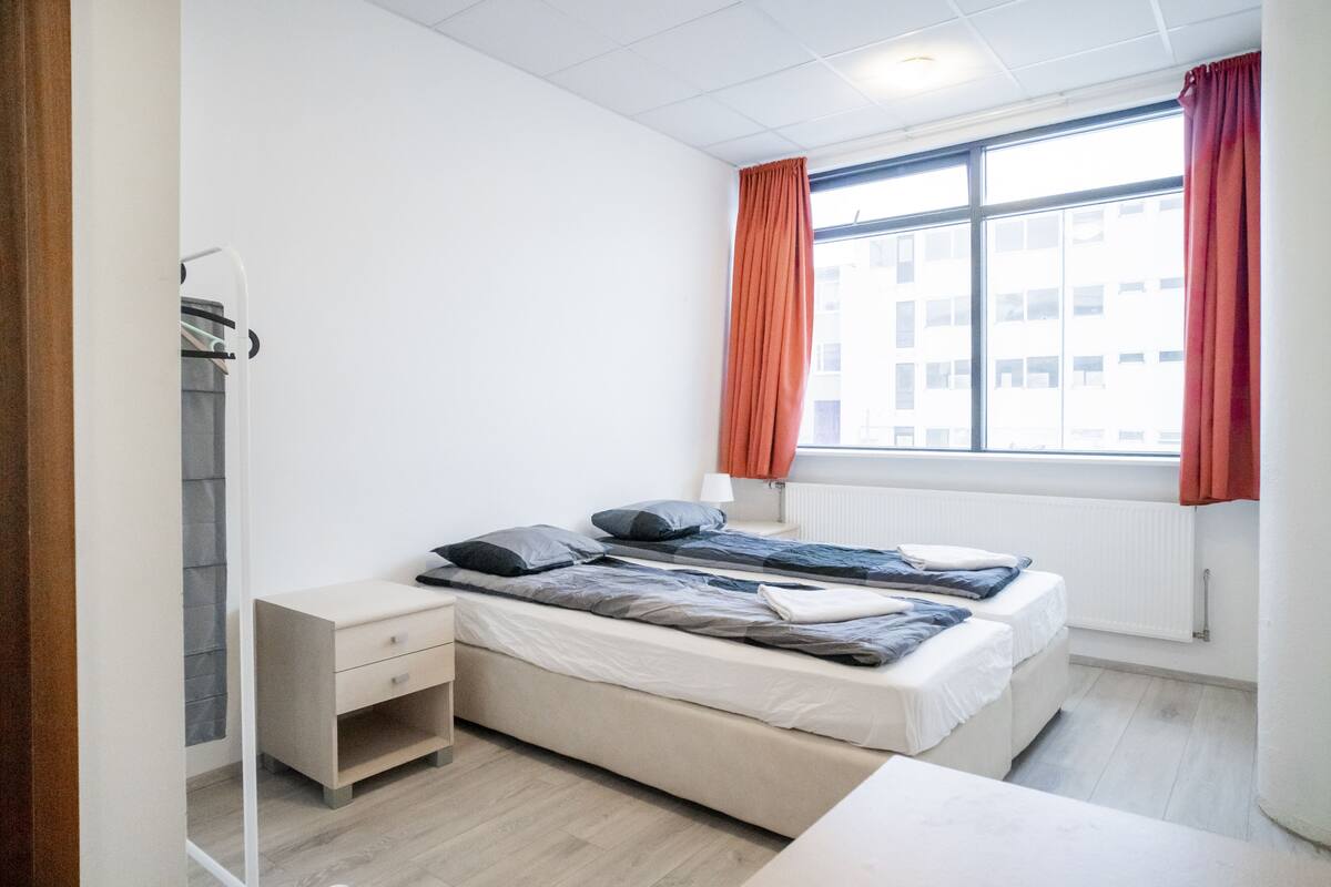 A bedroom with a bed, a bedside table, a wardrobe, and a window with curtains.
