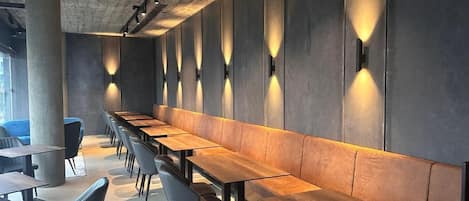 Un interior moderno con mesas de madera largas y sillas negras, techo de hormigón e iluminación empotrada.