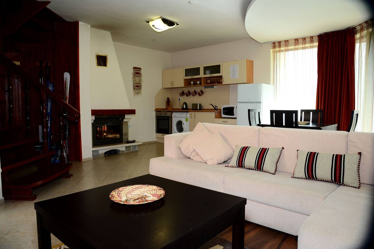 A living room with a sofa, a coffee table, and a fireplace. There is a kitchen area with a microwave and a stove.