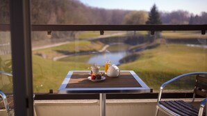 En balkon med et bord dækket til morgenmad, med udsigt over en flod og et skovlandskab.