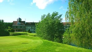 En golfbane med et klubhus, et flag og træer.