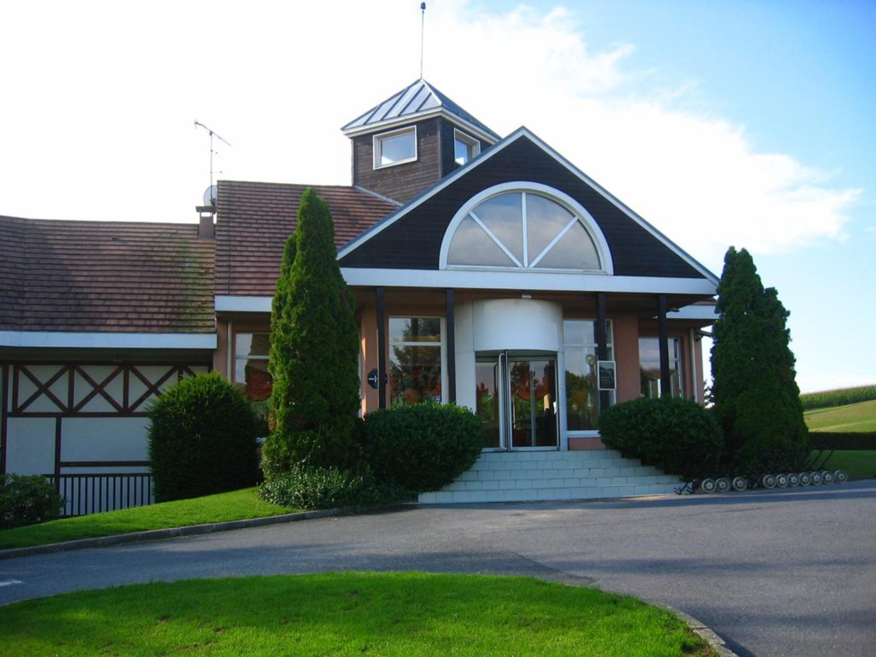 A modern building with a prominent entrance, a small tower-like structure, and a large arched window.