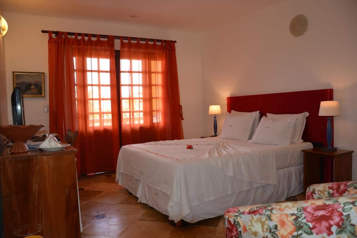 Une chambre à coucher avec un lit, deux lampes de chevet, une commode en bois et une fenêtre avec des rideaux.