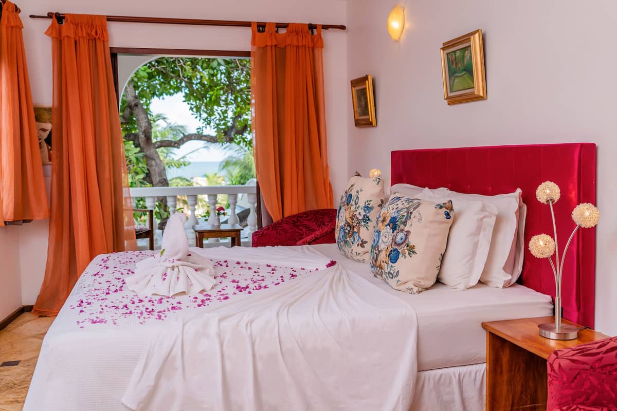 Une chambre d’hôtel avec un lit, une table de chevet, une tête de lit rouge et une vue sur l’extérieur.