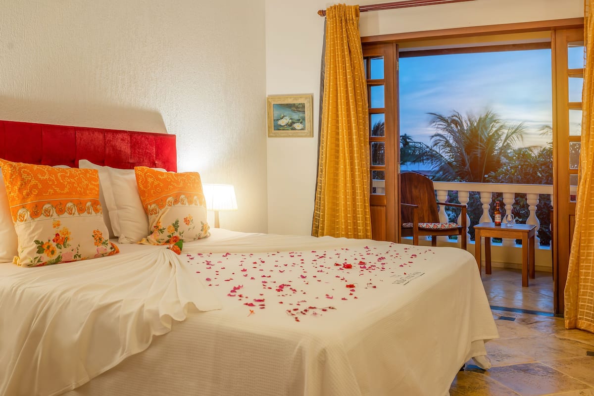 Une chambre d’hôtel avec un lit, une chaise, une table et un balcon donnant sur des palmiers.