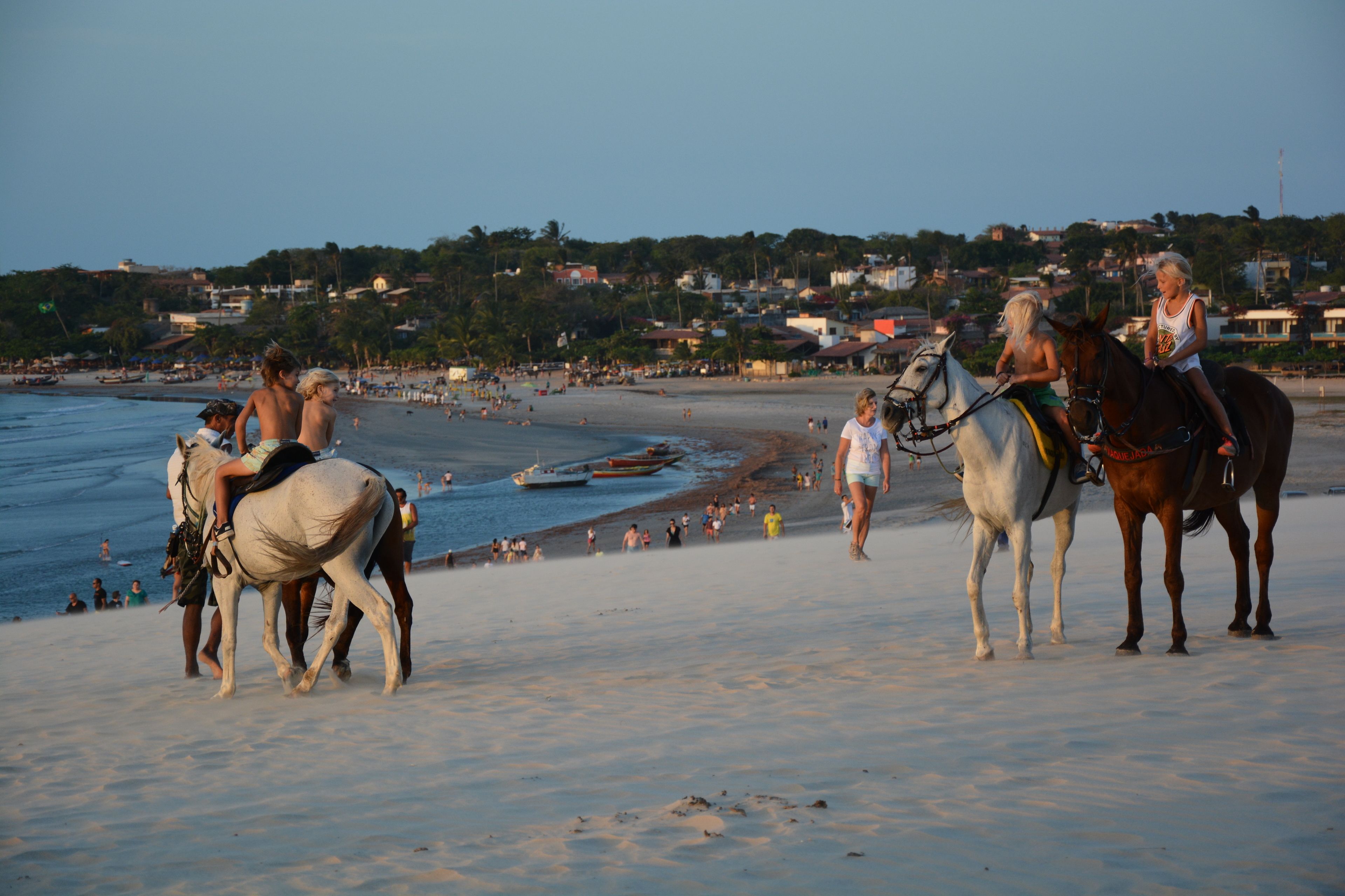 Una playa con gente montando a caballo y un barco en el agua.