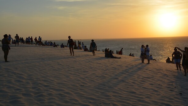 Een strand met mensen die over het zand lopen en zitten tijdens de zonsondergang.