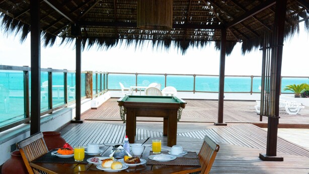 Une terrasse en bois avec une table dressée pour le petit-déjeuner, donnant sur une mer d’un bleu limpide.
