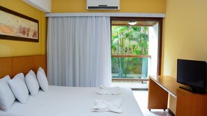 Une chambre d’hôtel avec un lit, des oreillers blancs, une télévision et un balcon donnant sur un paysage verdoyant.
