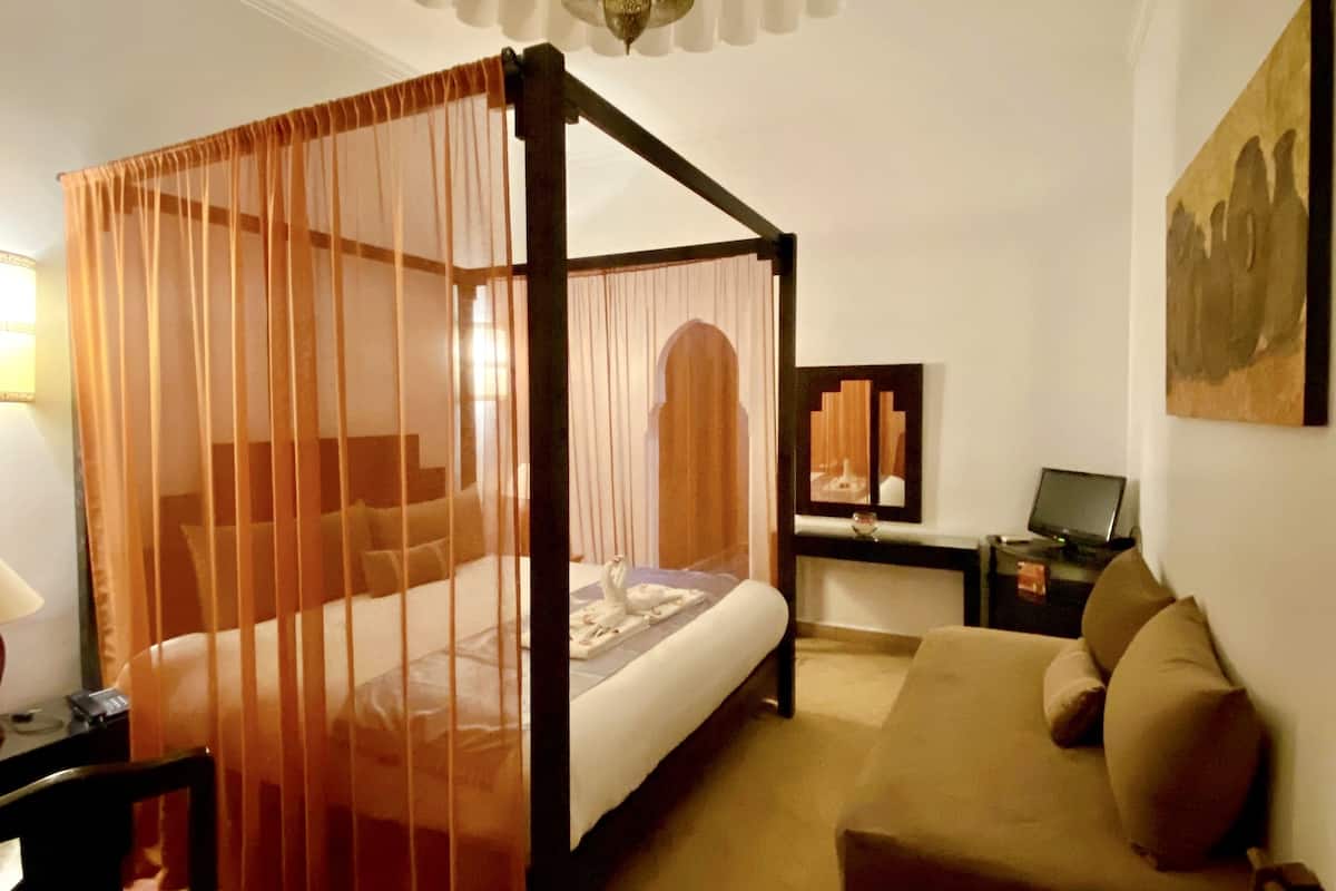 A four-poster bed with a canopy, a sofa, a desk with a lamp, and a painting on the wall.