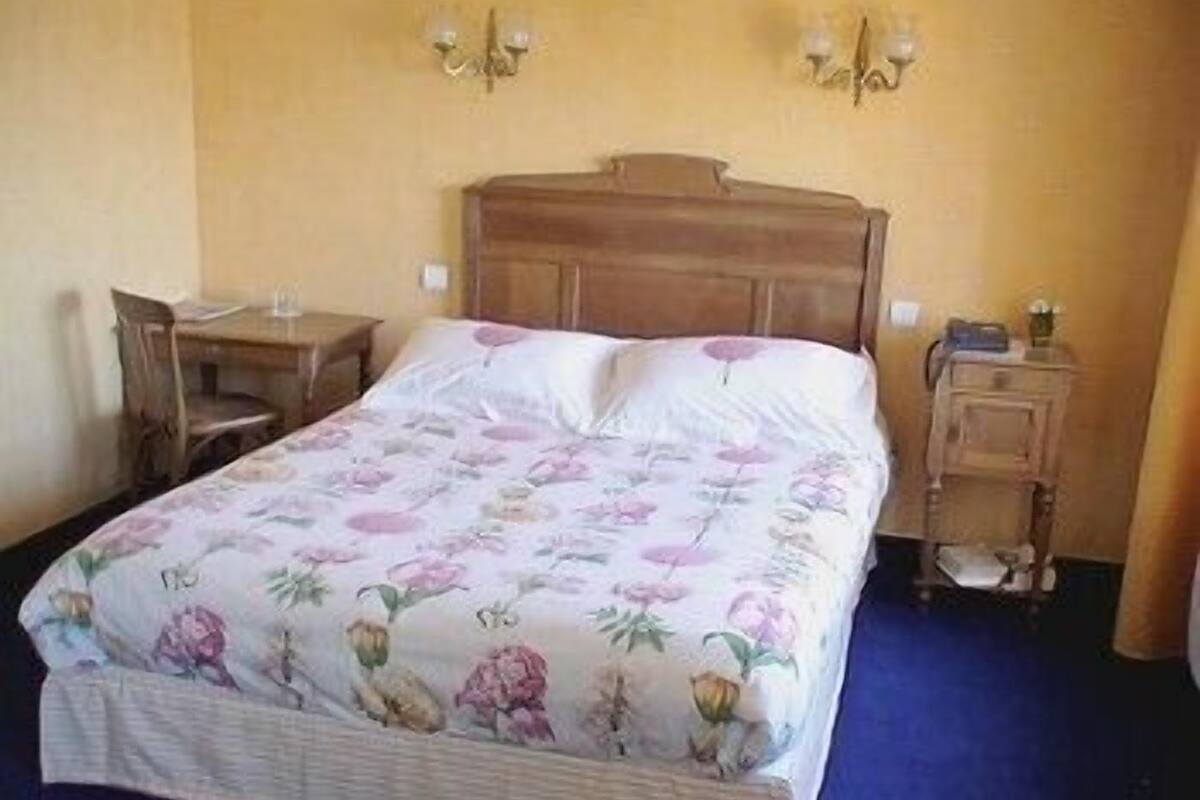Ein Schlafzimmer mit einem hölzernen Bett, floralem Bettzeug, einem Schreibtisch und einem Stuhl.