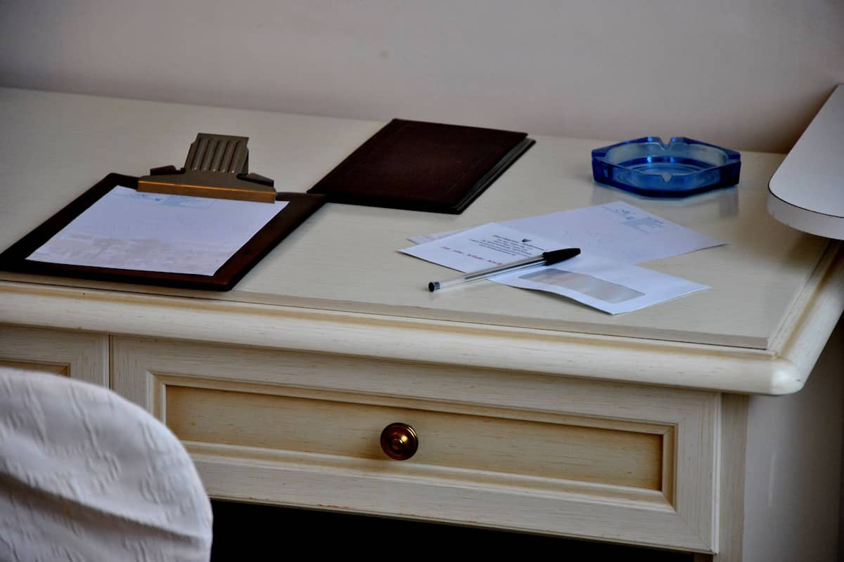 Un bureau avec un presse-papiers, des papiers, un stylo, un portefeuille et un cendrier bleu.