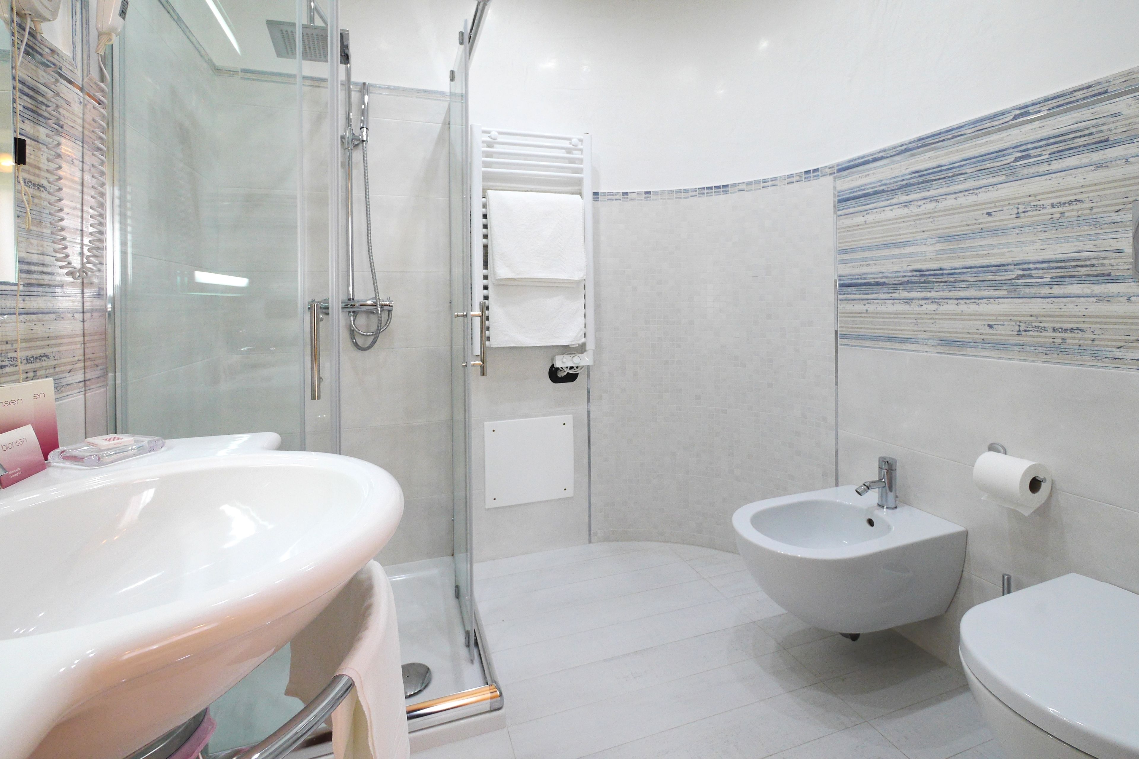 Un baño moderno con cabina de ducha de vidrio, un lavabo blanco, un bidé y un inodoro.