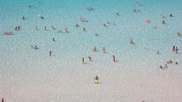 Een druk strand met mensen die zwemmen en zonnebaden.