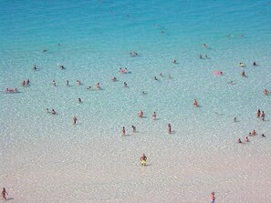 Una playa concurrida donde gente nada y toma el sol.