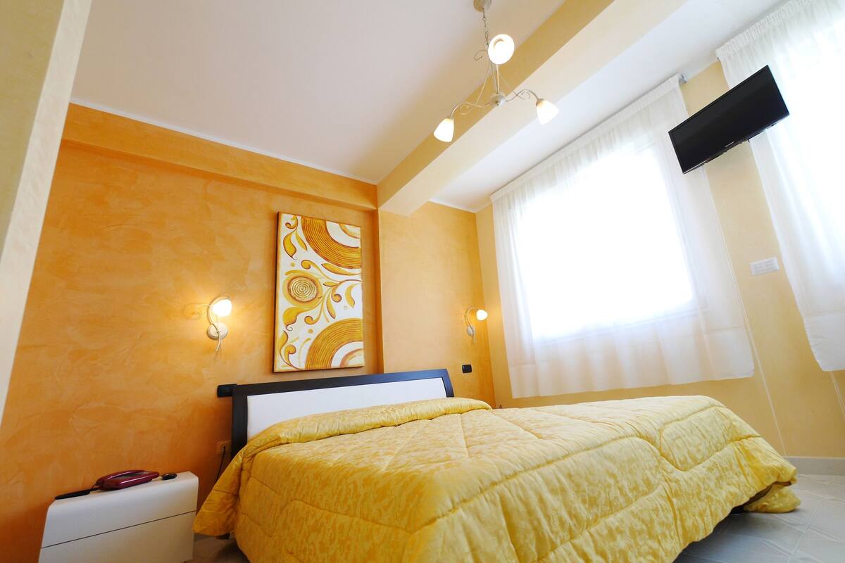 Une chambre à coucher comprenant un lit, une table de chevet, un téléviseur fixé au mur et une fenêtre avec des rideaux.