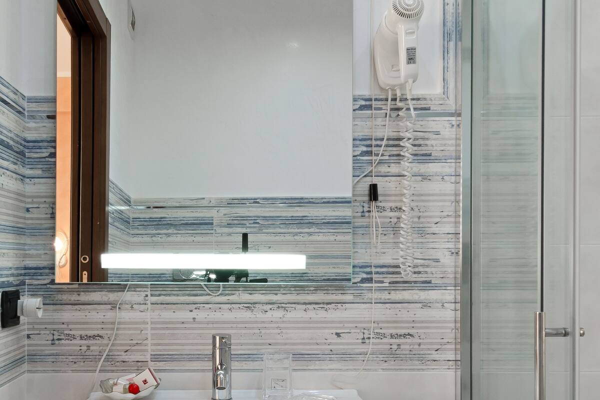 Une salle de bain moderne avec un grand miroir, un lavabo blanc et une cabine de douche en verre.