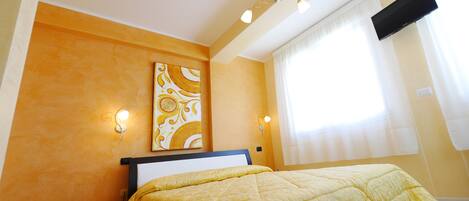 A bedroom with a bed, a nightstand, a wall-mounted TV, and a window with curtains.