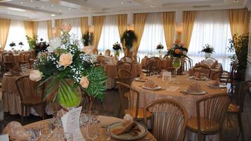 Un salón de banquetes con mesas redondas dispuestas para comer, cada una con un atril para el menú, copas de vino y centros de mesa florales.