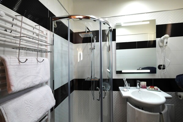 Un baño moderno con ducha de vidrio, lavamanos blanco y toallero con toallas.