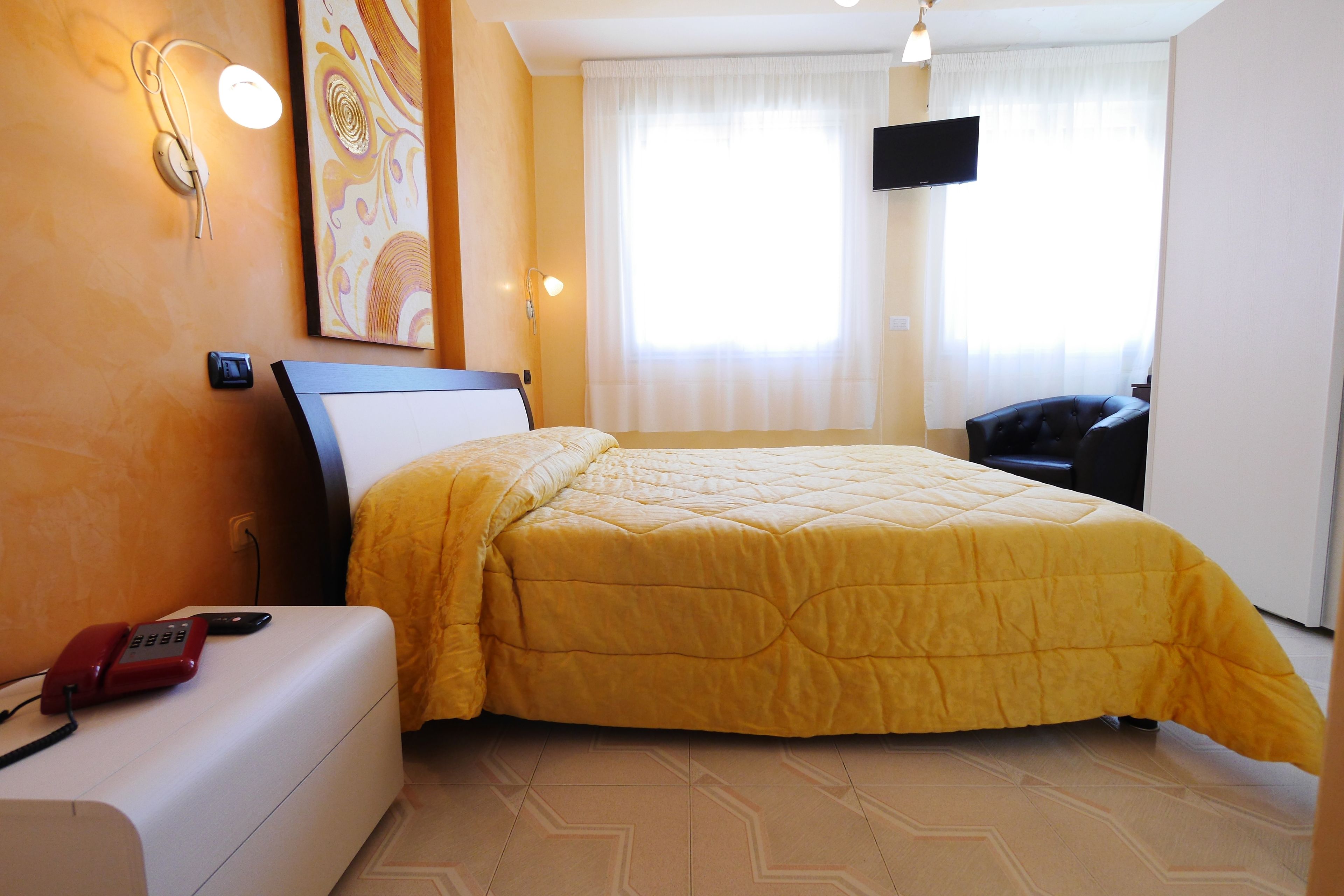 Habitación de hotel con cama, mesita de noche con teléfono, televisor montado en la pared y ventana con cortinas.