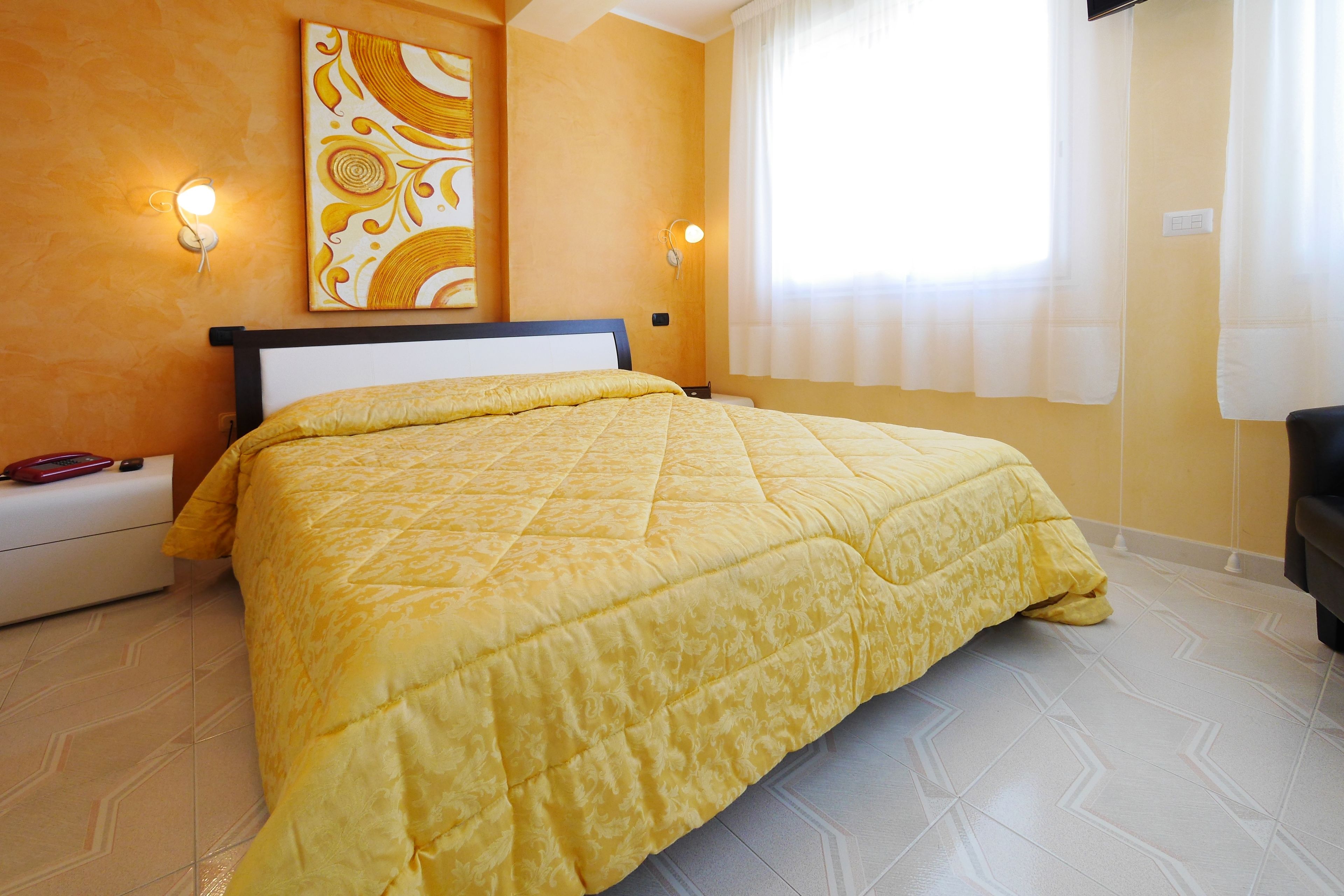 Habitación de hotel con cama, mesita de noche, lámpara de pared y ventana con cortinas.