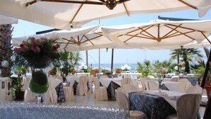 Een terras met tafels, stoelen, parasols en potplanten.
