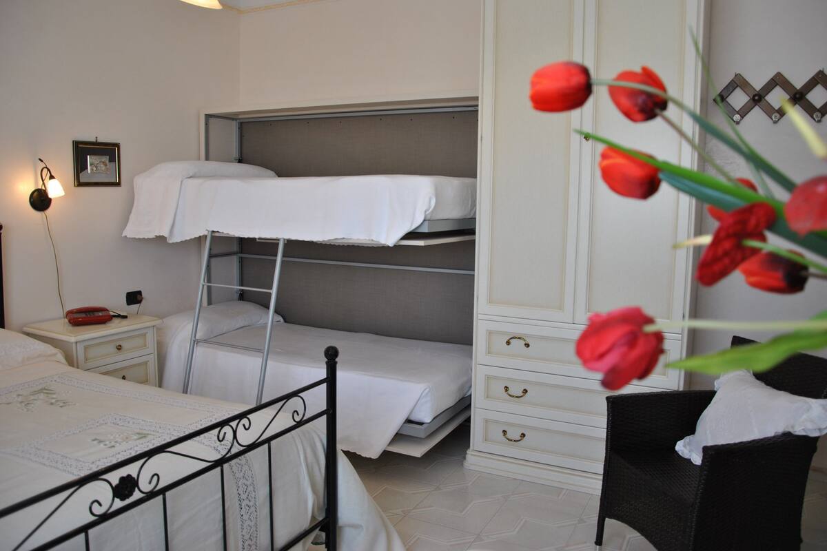 Une chambre avec un lit superposé, une table de chevet avec une lampe, une chaise et une armoire.