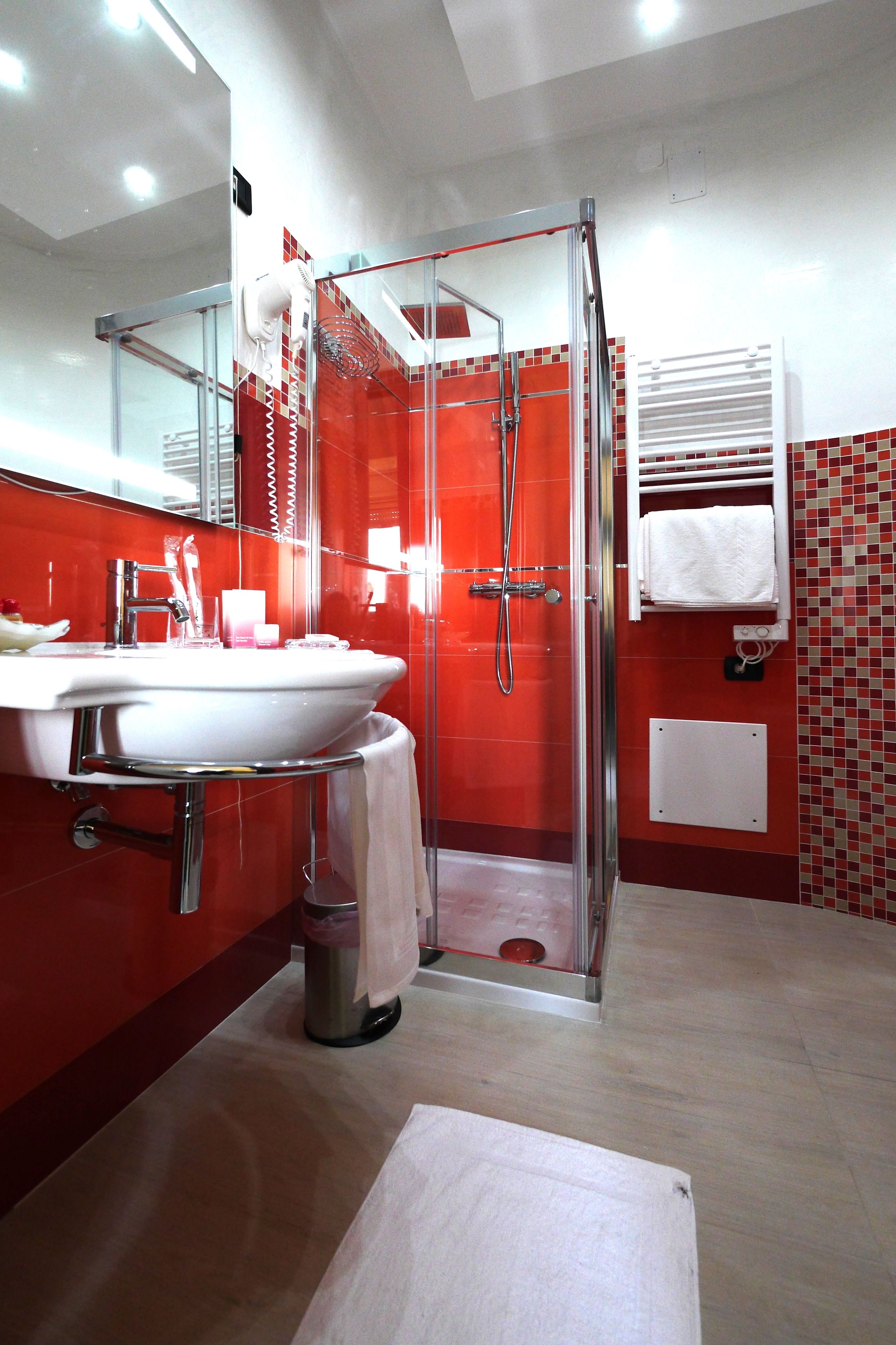 A modern bathroom with a glass-enclosed shower, a white sink, and a red-tiled wall.