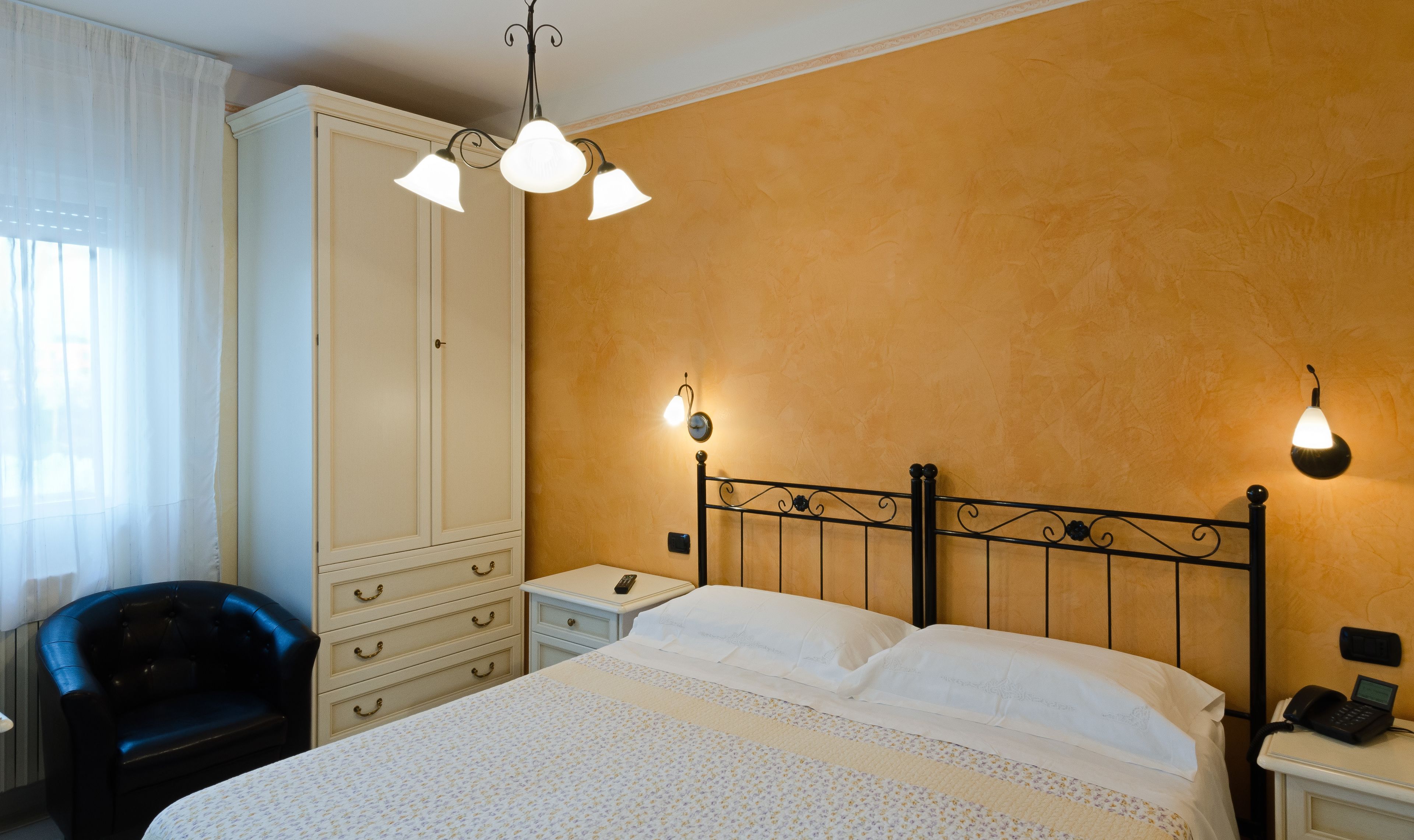 A hotel room with a bed, a wardrobe, a chair, and two bedside lamps.