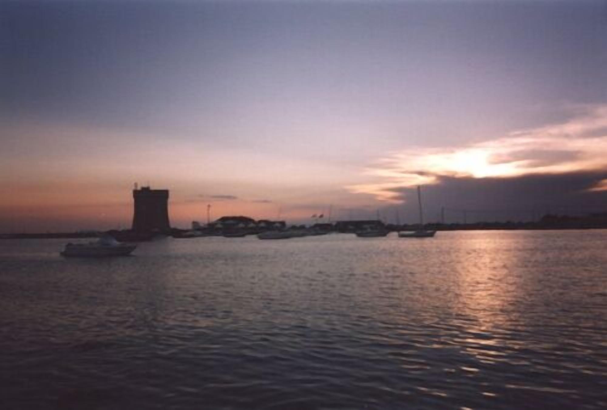 Un coucher de soleil sur un port, avec des bateaux et une tour.