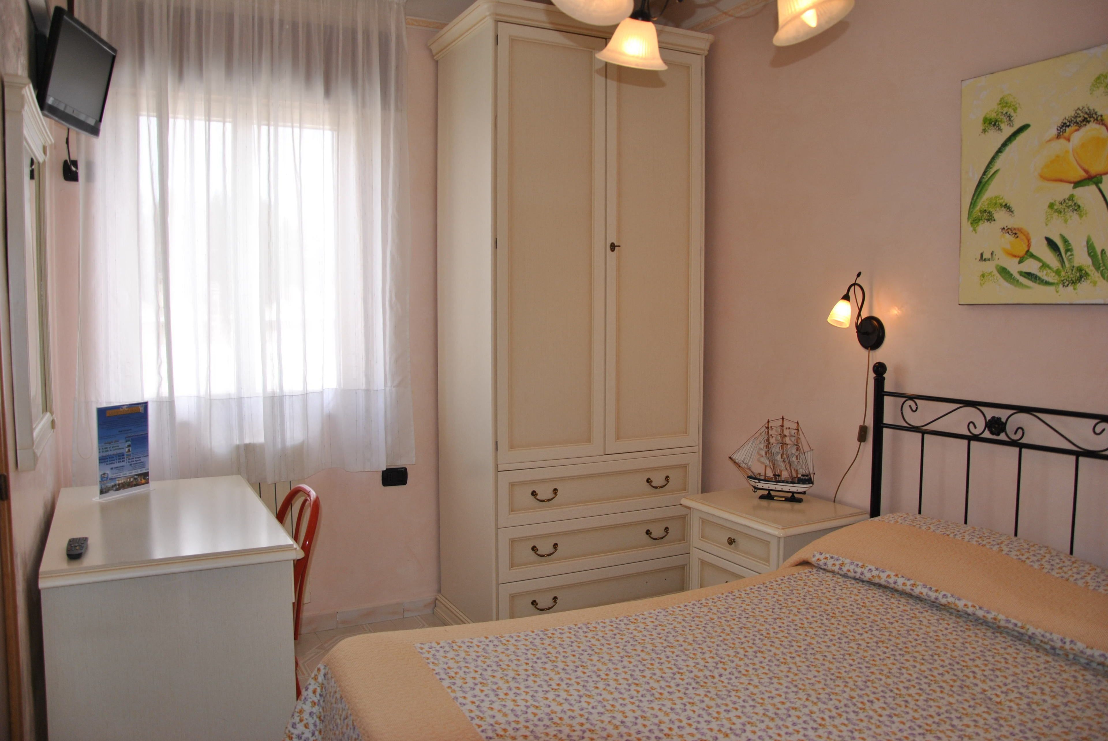Un dormitorio con cama, escritorio, armario, silla, mesita de noche y lámpara de pared.