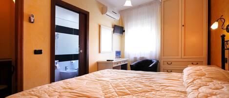 A hotel room with a large bed, a desk with a chair, a bathroom with a sink and mirror, and a wardrobe.