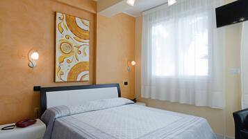 Habitación de hotel con cama, un cuadro en la pared, dos lámparas de pared, un televisor y una ventana con cortinas.