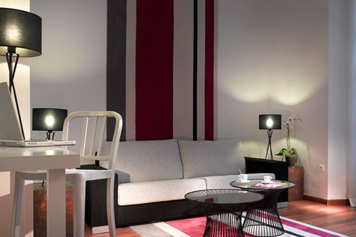 A modern living room with a sofa, a dining table, a laptop, two floor lamps, and a small table with a cup and saucer.
