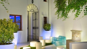A modern courtyard with a white building, a metal gate, potted plants, and white cylindrical seating. - Marquis Hotels Portago (Granada)