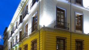 A multi-story building with a yellow facade and white upper levels, featuring balconies and large windows. - Marquis Hotels Portago (Granada)