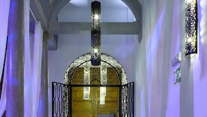 A hallway with a wooden door, black metal gates, and a reception desk with a vase of flowers. - Marquis Hotels Portago (Granada)