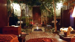 A cozy indoor garden with a central fire feature, surrounded by seating and potted plants. - Riad Jenaï Demeures du Maroc (Marrakech)