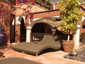 Un patio con una zona de estar cubierta, plantas en macetas y una maceta grande.