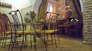 Un comedor con una mesa redonda y cuatro sillas, un florero con flores, y una pared con cuadros y utensilios de cocina.