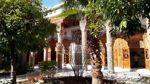 A courtyard with a fountain, palm trees, and a building with arches and columns. - Riad Jenaï Demeures du Maroc (Marrakech)