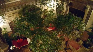 Un jardín interior con un sofá rojo, diversas plantas en macetas y una pequeña mesa con mantel rojo.