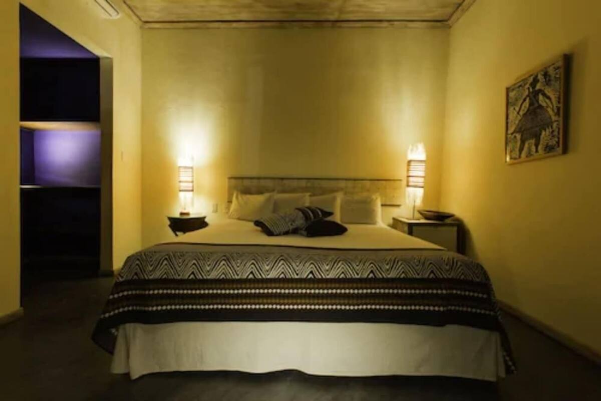 A single bed with a patterned bedspread, two bedside lamps, and a wall-mounted artwork.