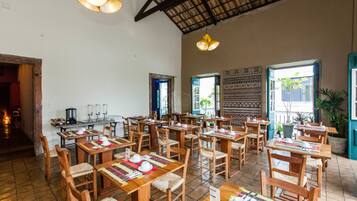 A restaurant with wooden tables and chairs, a tiled floor, and a high ceiling with exposed beams.
