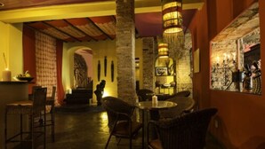 Un interior tenuemente iluminado con mobiliario de mimbre, pilares de piedra y una zona de bar con objetos decorativos.