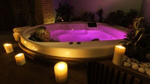 Un jacuzzi con una persona adentro, rodeado de velas y plantas.
