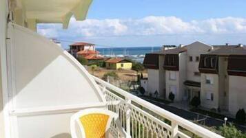 A balcony with a view of a coastal town, featuring buildings with red roofs and a clear sky.