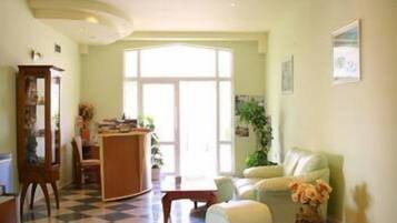 A living room with a checkered floor, a wooden desk, a white sofa, and a large window.