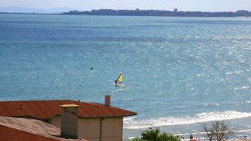 A coastal view with a clear sky, a person windsurfing, and a building with a red roof in the foreground.